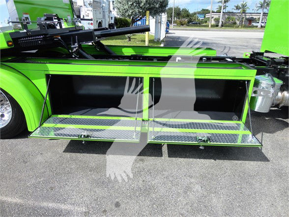 Truck body with open storage compartments on a bright green Peterbilt 337 tow truck side view showing two large hinged compartments with diamond plate steps.