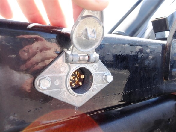 Ram 5500 HD hooklift truck component showing a circular outlet with multi-pin connector and hinged cover mounted on a black painted frame.