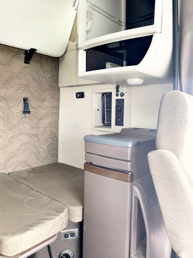 Interior cab area of a 2018 Volvo VNL 670 showing sleeper seat, small refrigerator, control panel, and overhead storage.