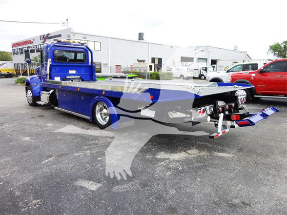 Blue Peterbilt 337 tow truck with a flatbed, viewed from the rear-left side; stock number J56627 FM visible in listing metadata.