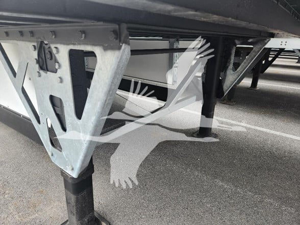 Trailer undercarriage showing metal frame with jack stands and support legs; visible are structural truss brackets and cross-members.