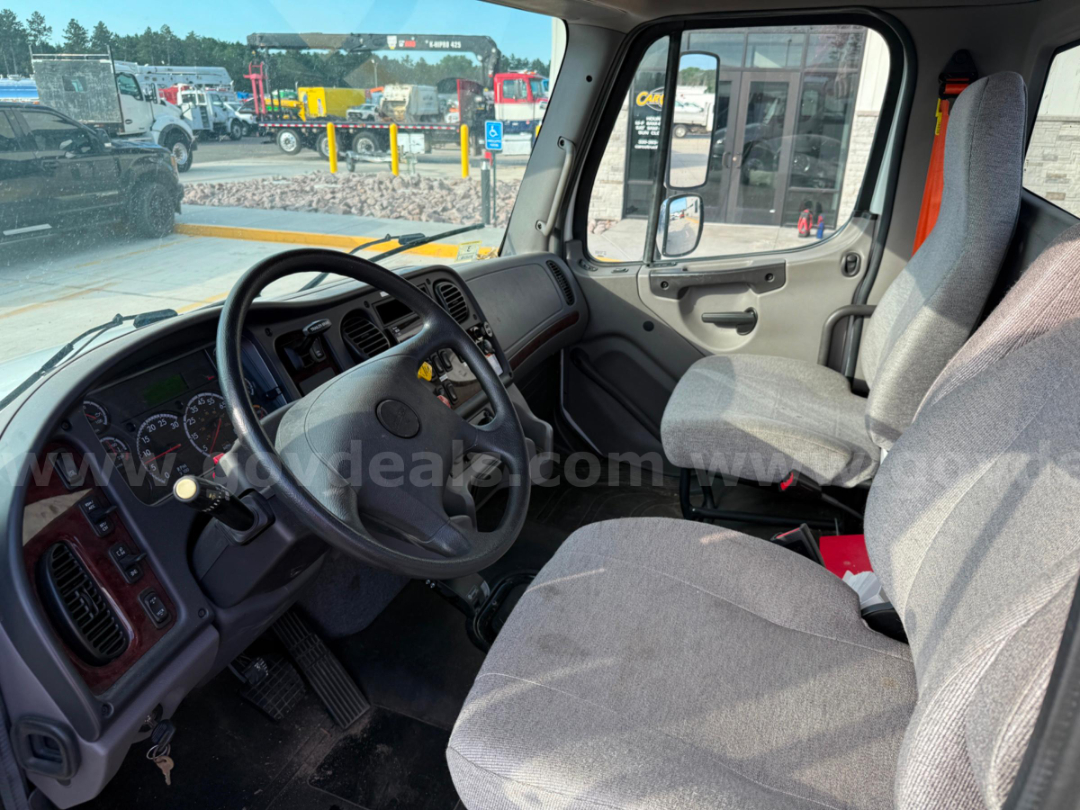 Truck cab interior showing steering wheel, instrument cluster, and gray fabric seats with driver and passenger seating in Freightliner TEREX TC-55 bucket truck.