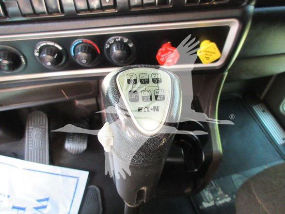 Kenworth W900L interior showing gear shifter with transmission diagram and three control knobs; red and yellow warning/indicator stickers near dash.