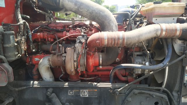 Truck engine bay showing red Peterbilt diesel engine with large intake hoses and turbo components.