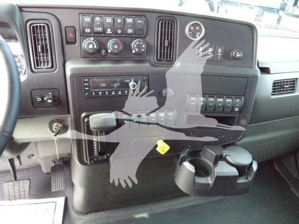 Truck dashboard showing steering column, control knobs, vents, digital clock, and cup holders with a watermark on the image.