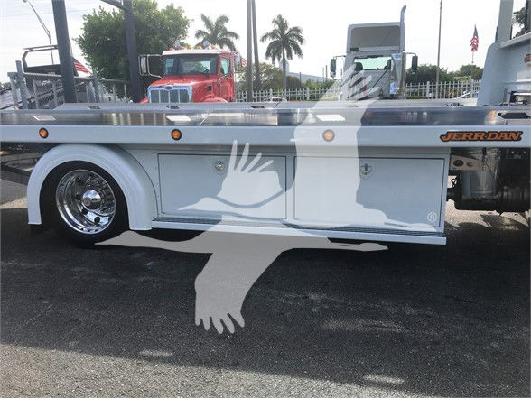 Tow truck side view showing white utility body with compartments on Peterbilt chassis, chrome wheel, Jerr-Dan branding on rear.