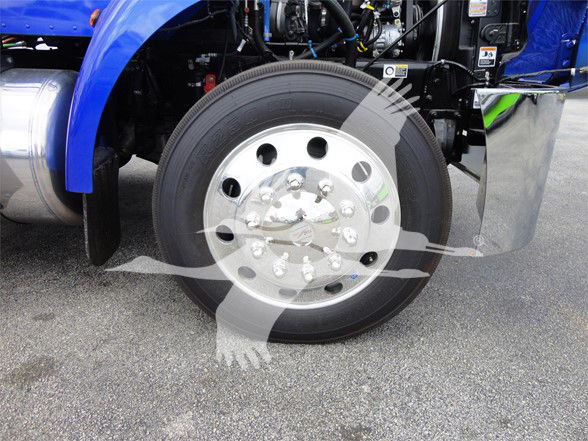 Peterbilt 337 front wheel and fender area showing large polished aluminum wheel with multiple lug nuts; blue tractor cab with engine bay components and chrome fuel tank visible.