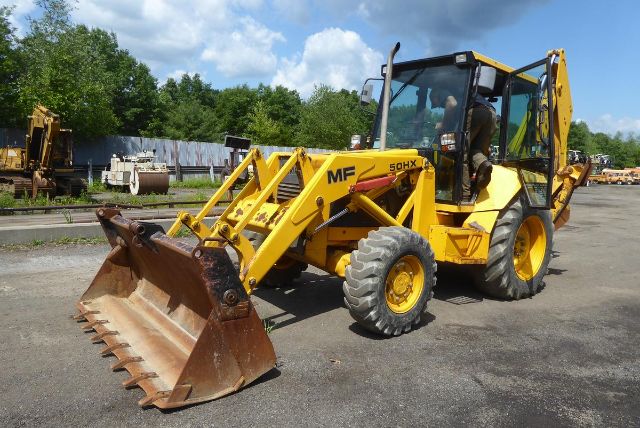 Yellow Massey Ferguson 50HX backhoe loader with front bucket and backhoe arm in a parking lot.
