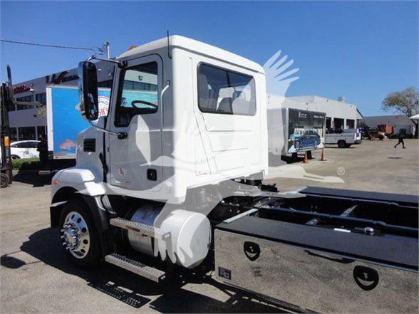 Truck cab of a 2024 Mack MD6 on display showing the driver's side with a white exterior and wheel, chassis behind the cab.