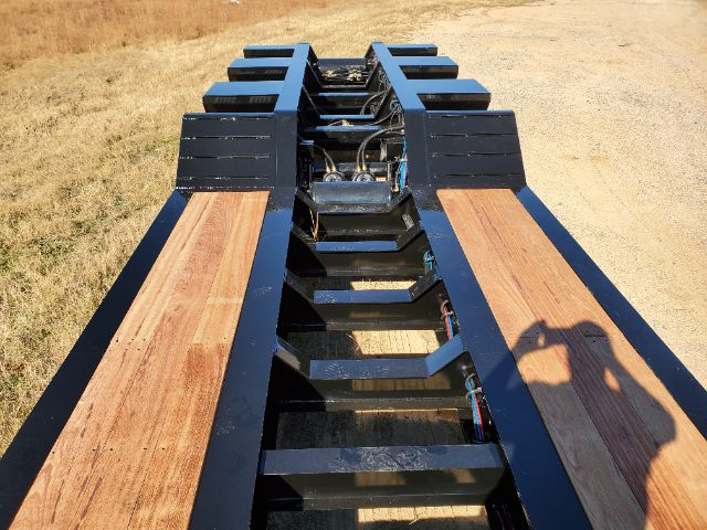 Lowboy trailer frame showing wooden deck sections and metal crossmembers with wiring harnesses in center.