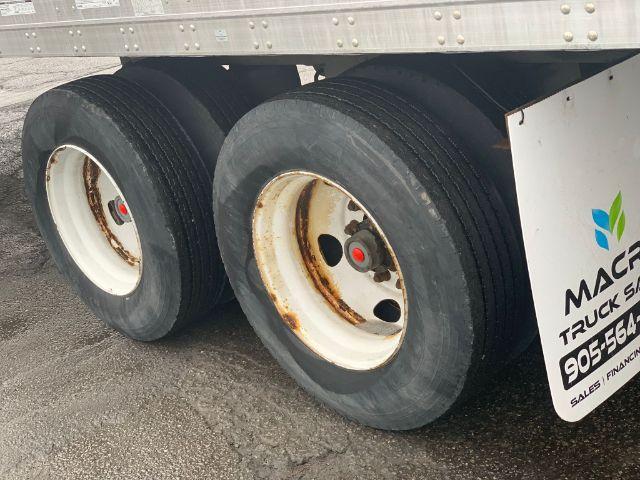 Dual rear wheels of a 2013 Stoughton dry van trailer showing rust on wheel rims and treaded tires. Partial side panel with Mack truck sign and contact digits visible.