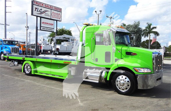 Green Peterbilt tow truck with flatbed in a dealership lot; visible text includes TLC Truck Sales Center sign and JERR D-AN? phone sign in background; Stock number J47210.