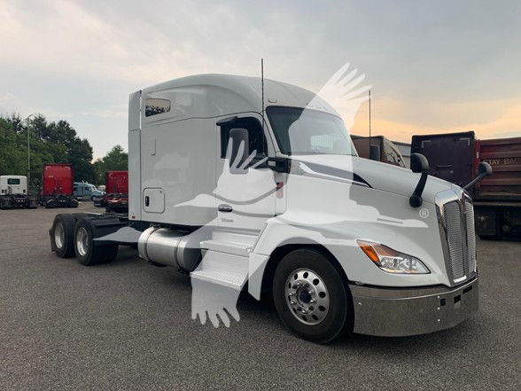 Kenworth T680 tractor unit in a light color with sleeper cab, showing front grille, headlights, and side steps. No visible text legible on the truck itself due to watermark.
