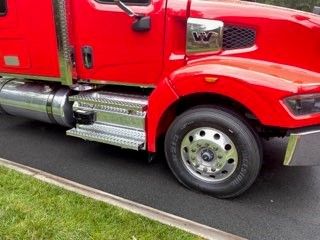 Truck side view showing chrome fuel tanks, step, and wheel on a red Western Star 4900 with silver accents.