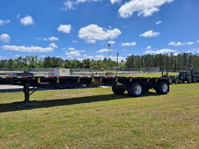 Flatbed trailer with dual rear axles and long flatbed showing Fontaine branding and reflective tape. Blue sky with scattered clouds.