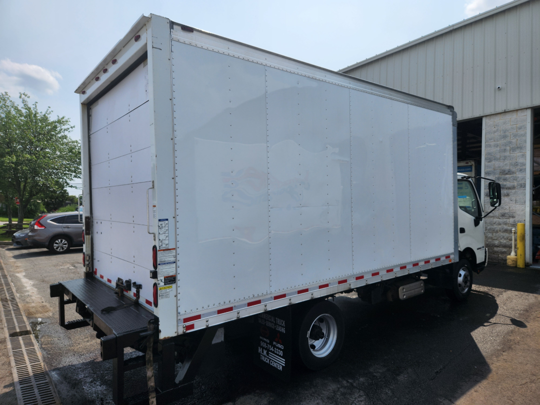 Side and rear view of a white 2017 Hino 155 box truck with cargo area, cab visible, and rear bumper platform.
