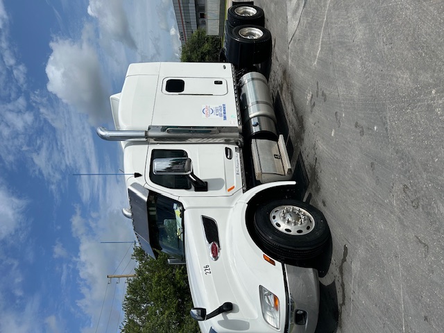 Peterbilt 579 conventional sleeper tractor, white, side view, chrome exhaust stacks, large fuel tanks, number 226 on hood, dual rear axles, shiny wheels.