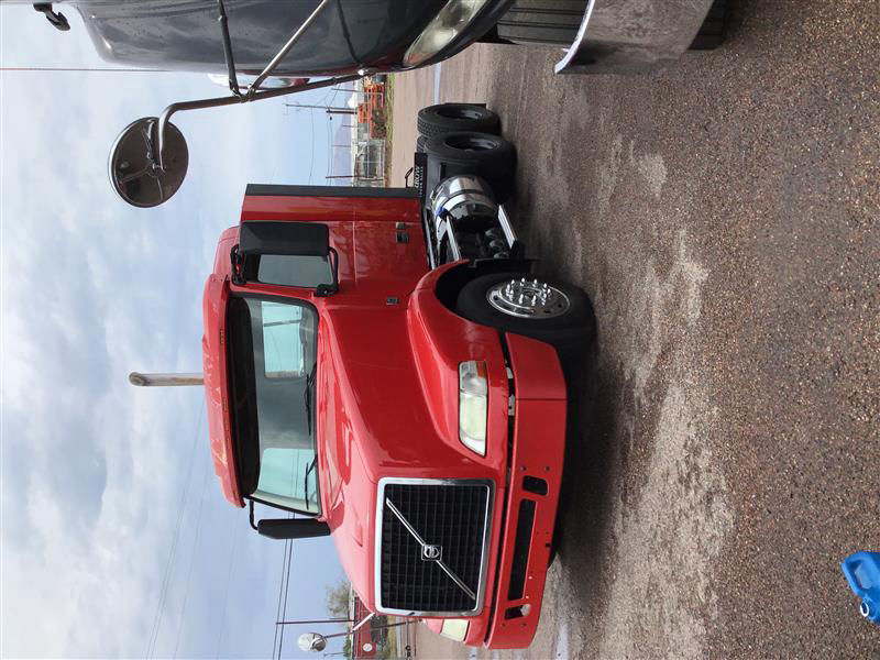 Volvo VNM64T-200 conventional daycab truck in red with grille and headlights, wheel, and side mirror visible.