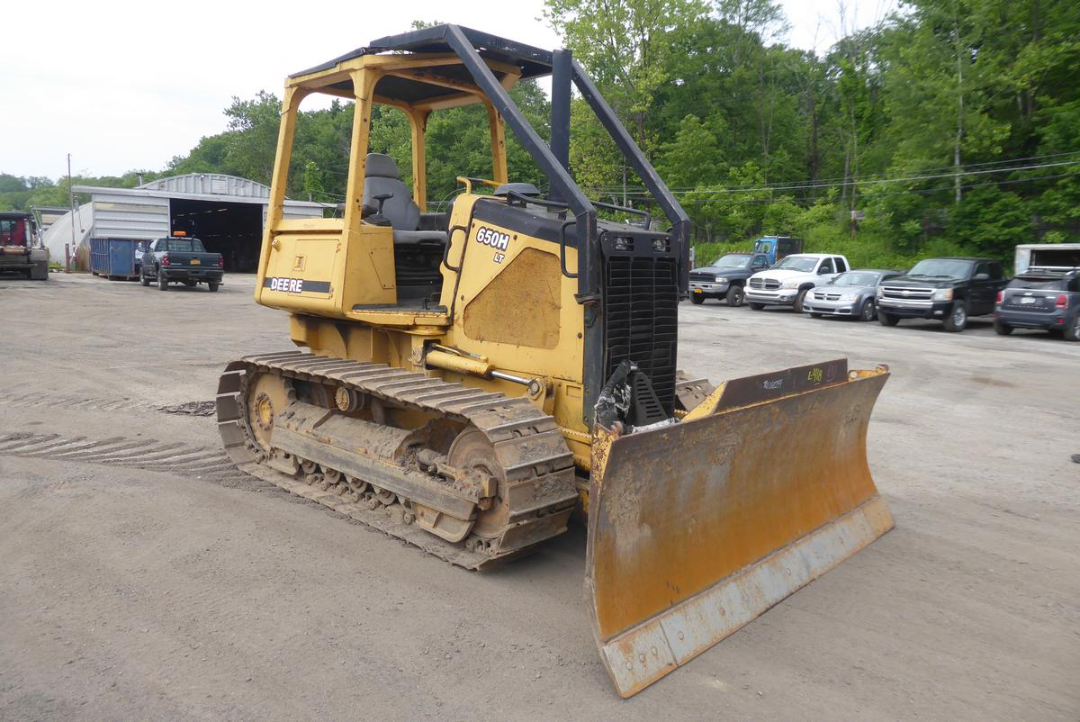 John Deere 650HLT crawler dozer with front blade, side view showing tracks and operator cab, yellow paint, dusty surface.