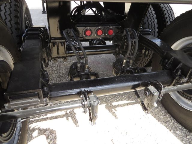 Rear undercarriage of a new trailer showing suspension arms, leaf springs, and a black frame with three red/black circular connectors on a plate between the wheels.
