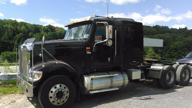 Truck cab with chrome front and black sleeper, International 9900i, side fuel tanks visible, logo mirrors, 6-wheel tractor with rear axles.