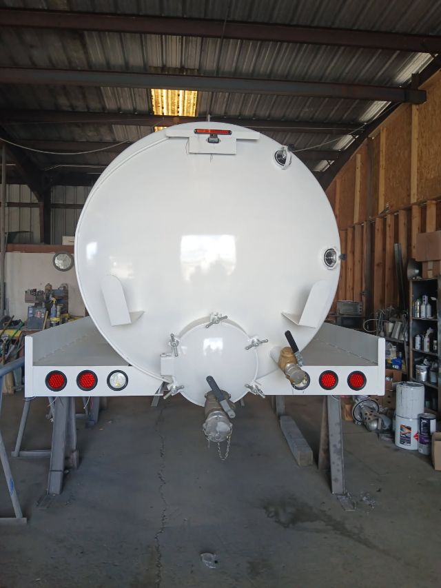 Rear view of a white 3500 gallon double baffled vacuum tank trailer inside a workshop, showing rear hatch, hoses, and taillights.