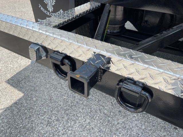 Rear bumper area of a 2013 Freightliner M2 showing a square hitch receiver and two circular towing loops on a black steel bumper with diamond plate step.