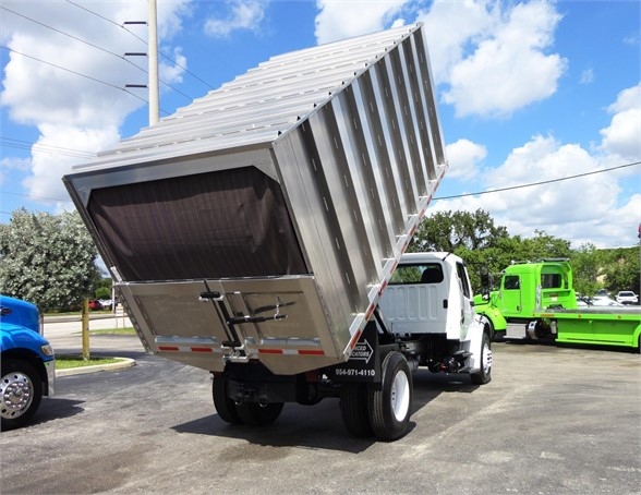 Truck bed of a Freightliner BUSINESS CLASS M2 106 dump truck in raised position with blue sky and other trucks in background.
