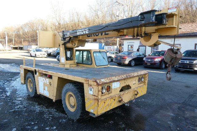 Grove YB4410 crane truck in service showing yellow machinery with onboard crane arm and hook, rear counterweights, and cabin window; visible wear on body.