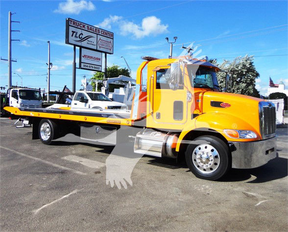 2022 Peterbilt 337 tow truck with bright yellow cab and flatbed, front chrome bumper, side mirrors, and a TLC sign in the background.