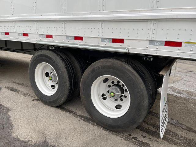 Partial side view of a Hyundai dry van trailer showing dual rear wheels, silver rim, black tires, and a white mudflap. Small Hyundai logo visible on side.
