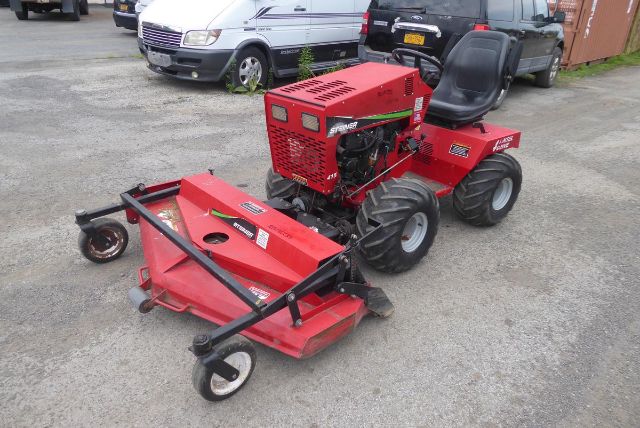 Red Steiner 415 utility tractor with mower attachment in a gravel lot, black roll bars, engine exposed, two large rear tires and a seat.