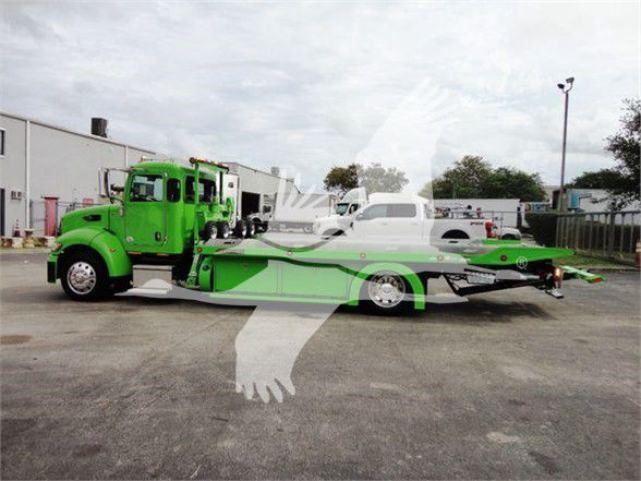 Green Peterbilt 337 tow truck with car hauler trailer in lot. Side shows Peterbilt cab and flatbed trailer; no legible text visible on logos or signs.
