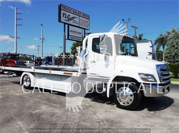 White 2022 Hino 268A tow truck with flatbed, side view showing cab and wheel, dealership lot in background.