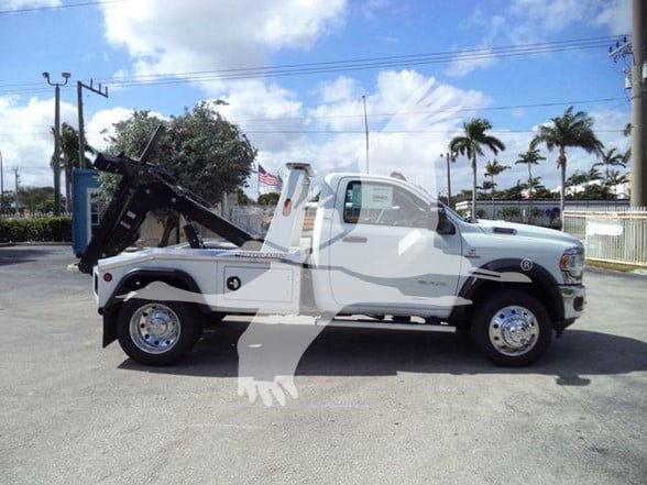 Ram 5500 tow truck side view with flatbed and crane, white color, two-tone chrome wheels, side steps. visible text not legible.