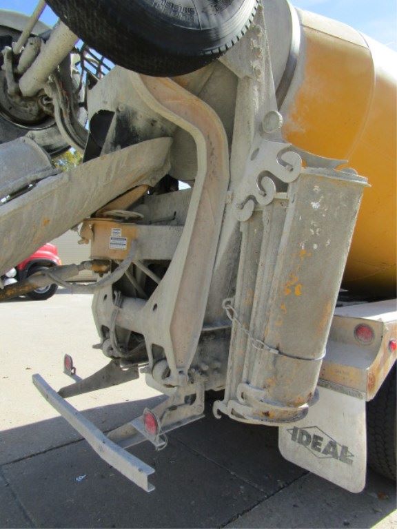 Back of a concrete pump truck showing platform, support frame, and stabilizer with ID tags, mud flaps, and hydraulic hose routing.