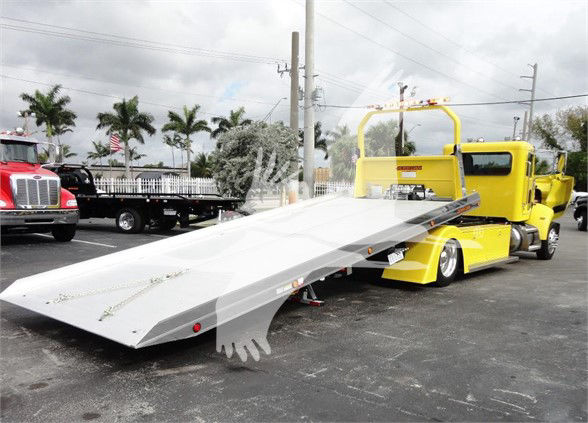 Tow truck with a bright yellow body and a long flatbed platform extending from the rear, ready for loading.