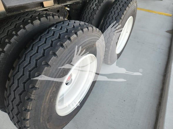 Truck trailer tires with white rims on a dual-axle dump trailer. Visible tread pattern and wheel wells; partial trailer frame above.