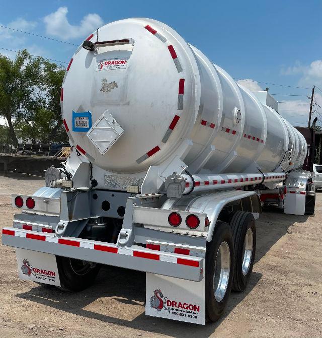 Crude oil tanker trailer rear view showing aluminum DOT-407 tank and dual-axle setup with red-and-white safety stripes.