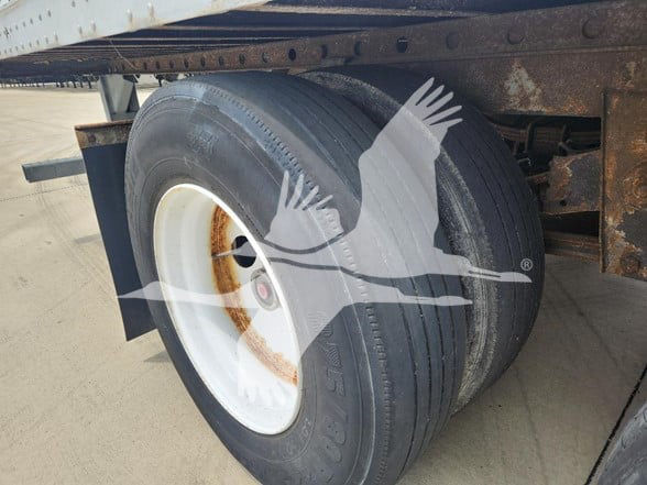 Great Dane trailer wheel and dual tire setup showing white steel rim with rusted hub area under a flatbed trailer.