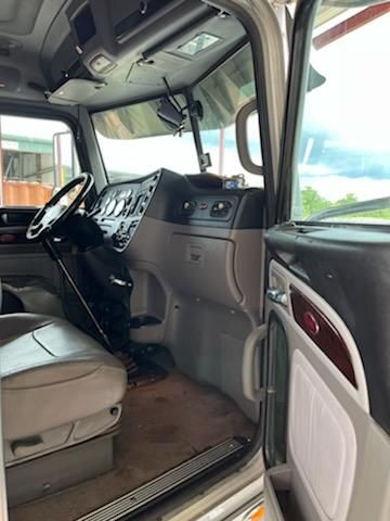 Truck cab interior view of a 2015 Peterbilt conventional sleeper with steering wheel, dashboard, and entry door visible.