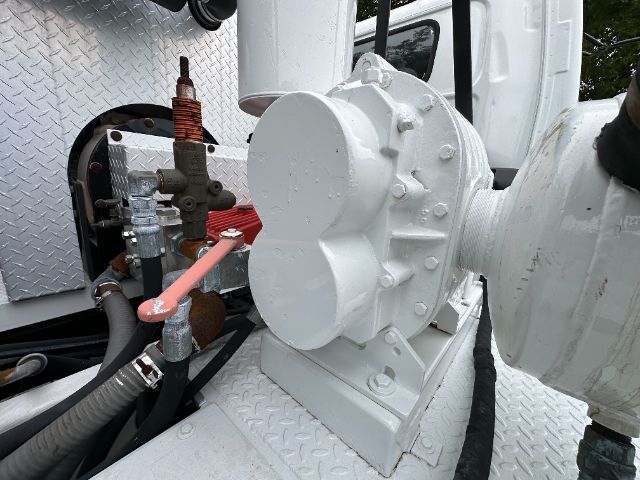 GMC W5500 vacuum truck component with large white pump/gear housing, hoses, and valves mounted on diamond plate platform.