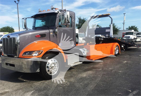Peterbilt 337 tow truck with orange and gray color scheme, flatbed with winch, chrome detailing, large front bumper, daylight, dealership lot in background.