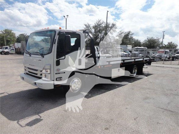 Isuzu NRR tow truck body with flatbed and wheel-lift equipment, front grille and cab visible, light traffic yard background.