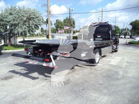 Tow truck with flatbed in rear, International MV truck, rear equipment and lights visible.