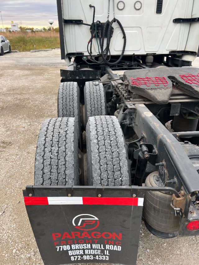 Tractor-trailer rear view showing dual rear axles and Paragon Freight Inc mudguard with contact info.