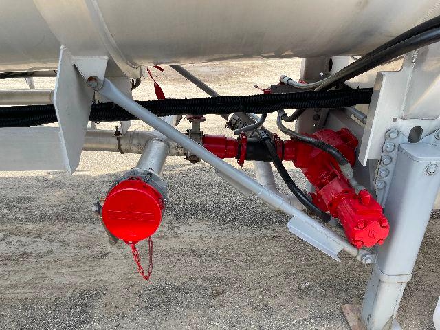 Crude oil trailer undercarriage showing aluminum DOT-407 tank, red valves, pipes, and support legs.