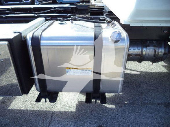 Close-up of a metal fuel or auxiliary tank mounted under a truck, with a warning label and metal strap brackets visible.