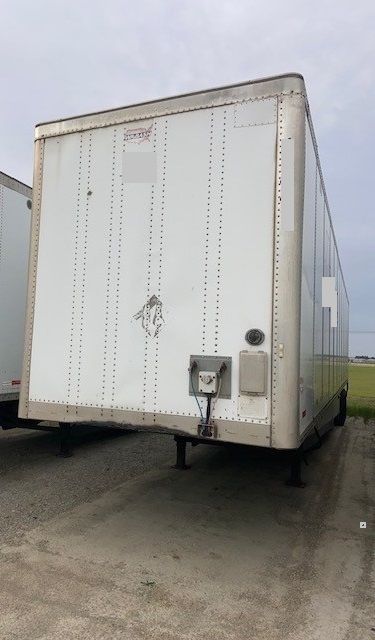 Trailer rear view showing white riveted cargo box with kingpin and connection hardware, corner brackets, and tandem axle undercarriage visible.