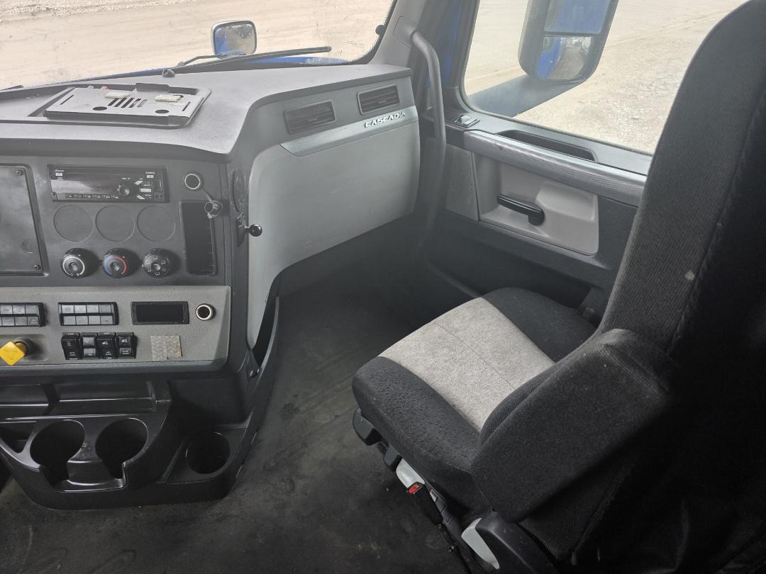 Cab interior of a 2018 Freightliner Cascadia truck showing dashboard with steering column, radio, climate controls, cupholders, and passenger seat.